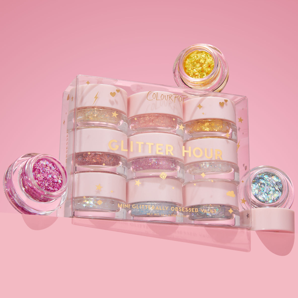 Glitter Hour ColourPop Glitter Gel Mini Glitterally Obsessed vault showcasing nine mini jars in a clear starry box, with open pots revealing gold, pink, and blue chunky sparkles on a pastel pink background.