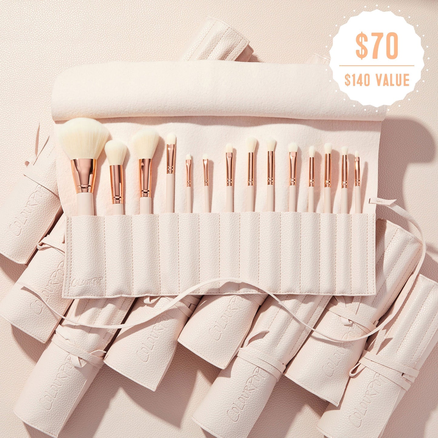 Sweet Fantasy ColourPop Shadow Palette & Brush Set brush roll opens to reveal soft white-bristle face and eye brushes with rose-gold ferrules, arranged in a blush-pink travel case on a textured nude surface, with a $70 ($140 value) badge.