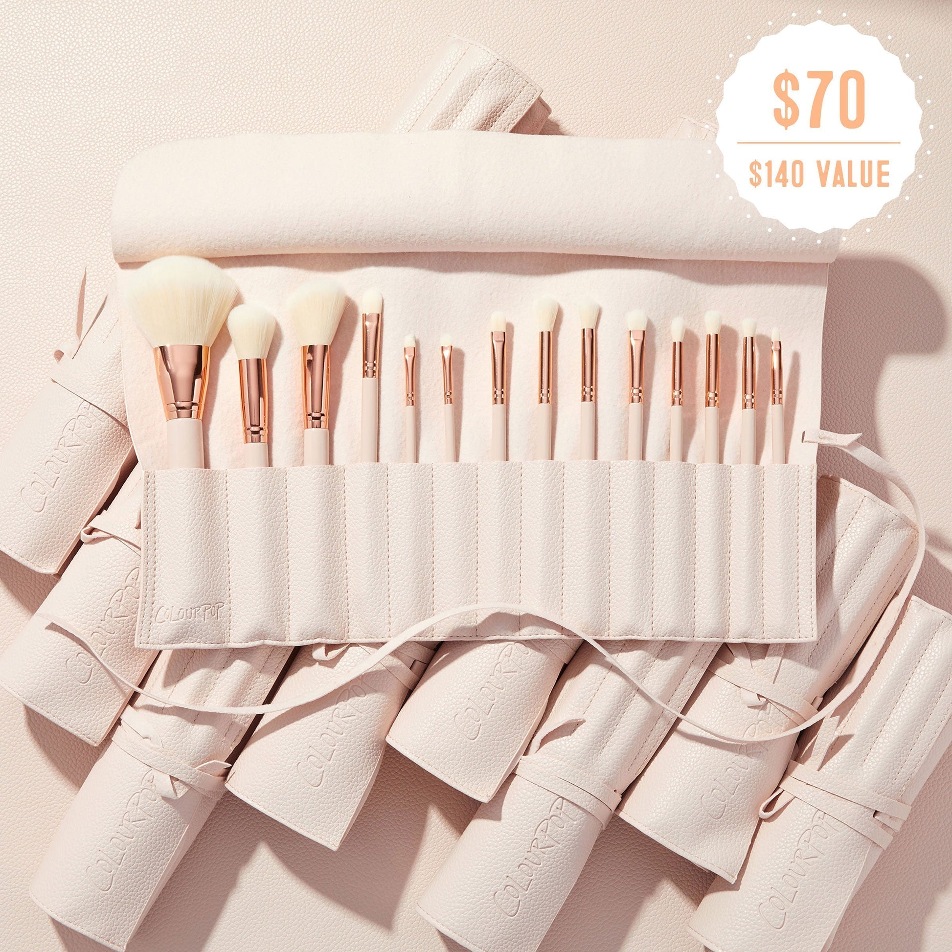 Sweet Fantasy ColourPop Shadow Palette & Brush Set brush roll opens to reveal soft white-bristle face and eye brushes with rose-gold ferrules, arranged in a blush-pink travel case on a textured nude surface, with a $70 ($140 value) badge.