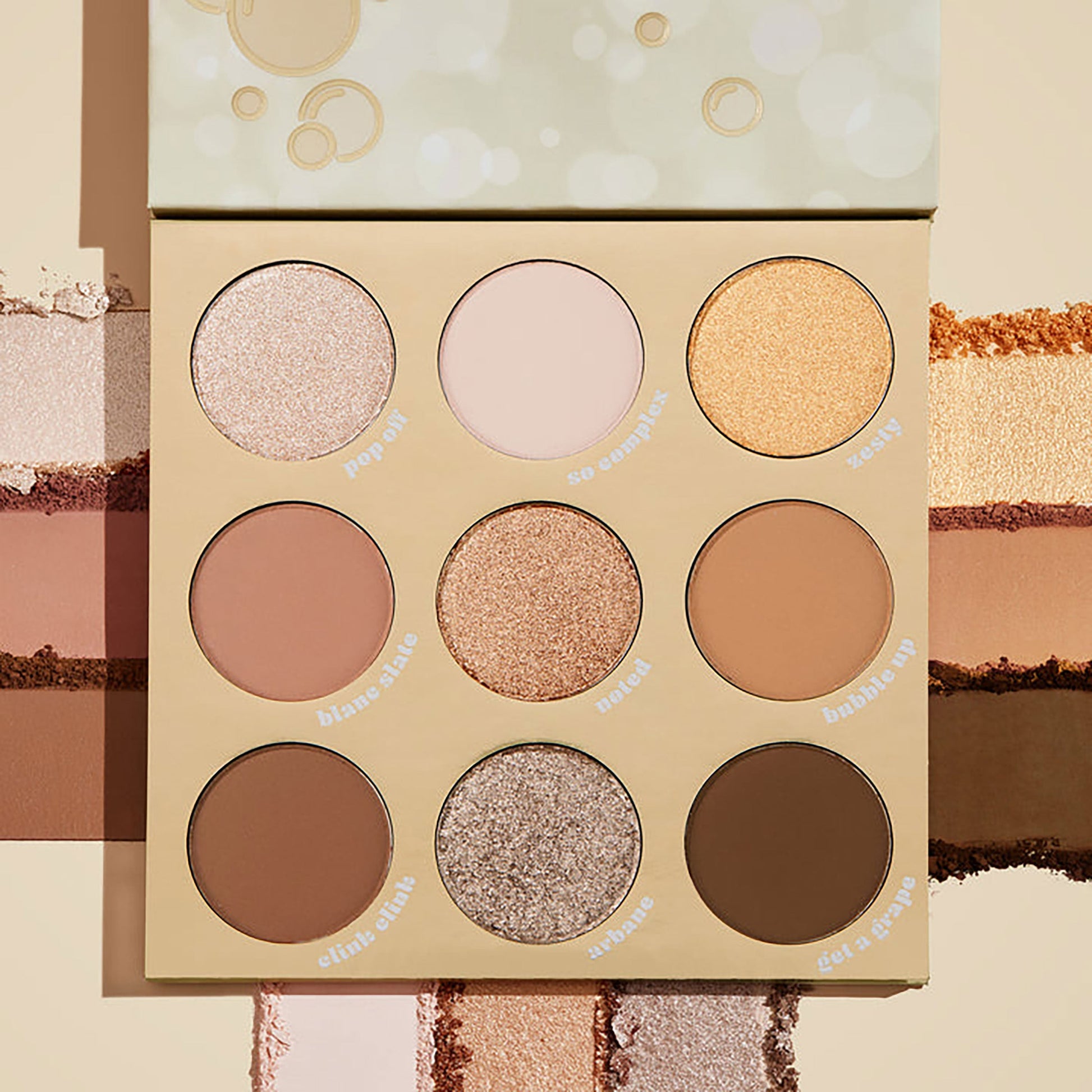 ColourPop Feelin' Bubbly shadow palette open, showing a 9-pan range of champagne, gold, taupe, and brown shades in matte and shimmer finishes, set on a cream backdrop with pigment swatches and bubbly-themed beige packaging.