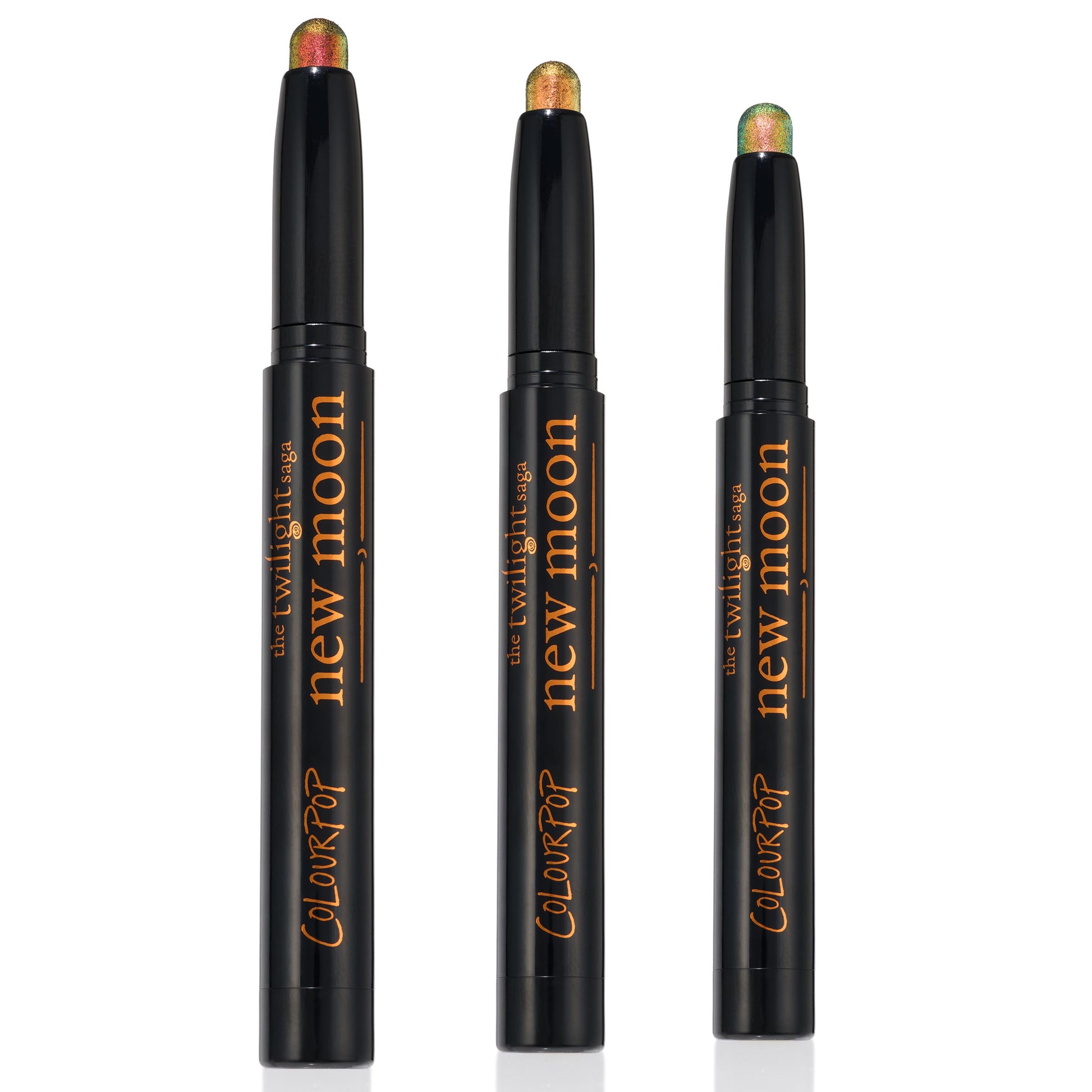 Love Triangle trio of ColourPop Shadow Stix stand uncapped to display shimmery multichrome tips - copper-red, golden bronze, and green-teal - in sleek black twist-up pens with The Twilight Saga New Moon branding, set against a clean white background.
