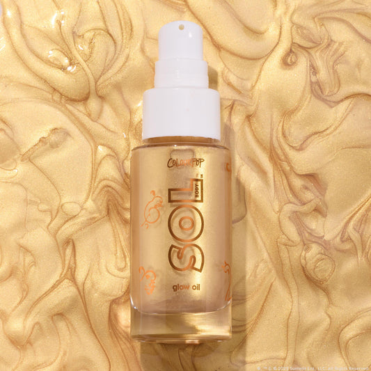 Clear glass bottle of ColourPop SOL Glow Oil, It’s a Wolf Thing, standing upright with a white pump and gold SOL logo, showcasing shimmering golden body oil against a swirled metallic gold backdrop.