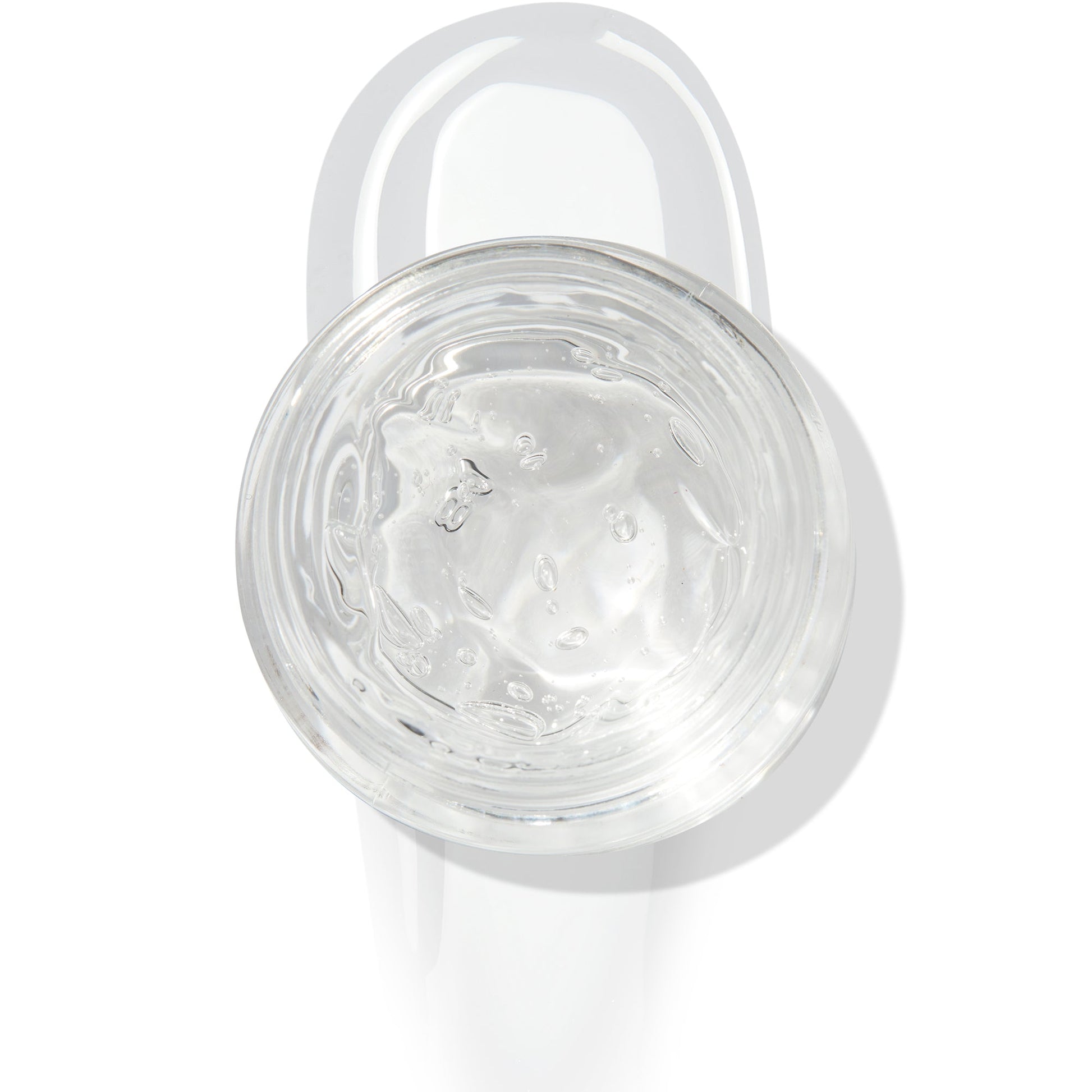 In The Clear Face & Eye Gloss in an open round jar gleams with a glossy swipe beneath it on a white background, showcasing the ColourPop Face & Eye Gloss for dewy, glass-skin shine on lids and cheeks.