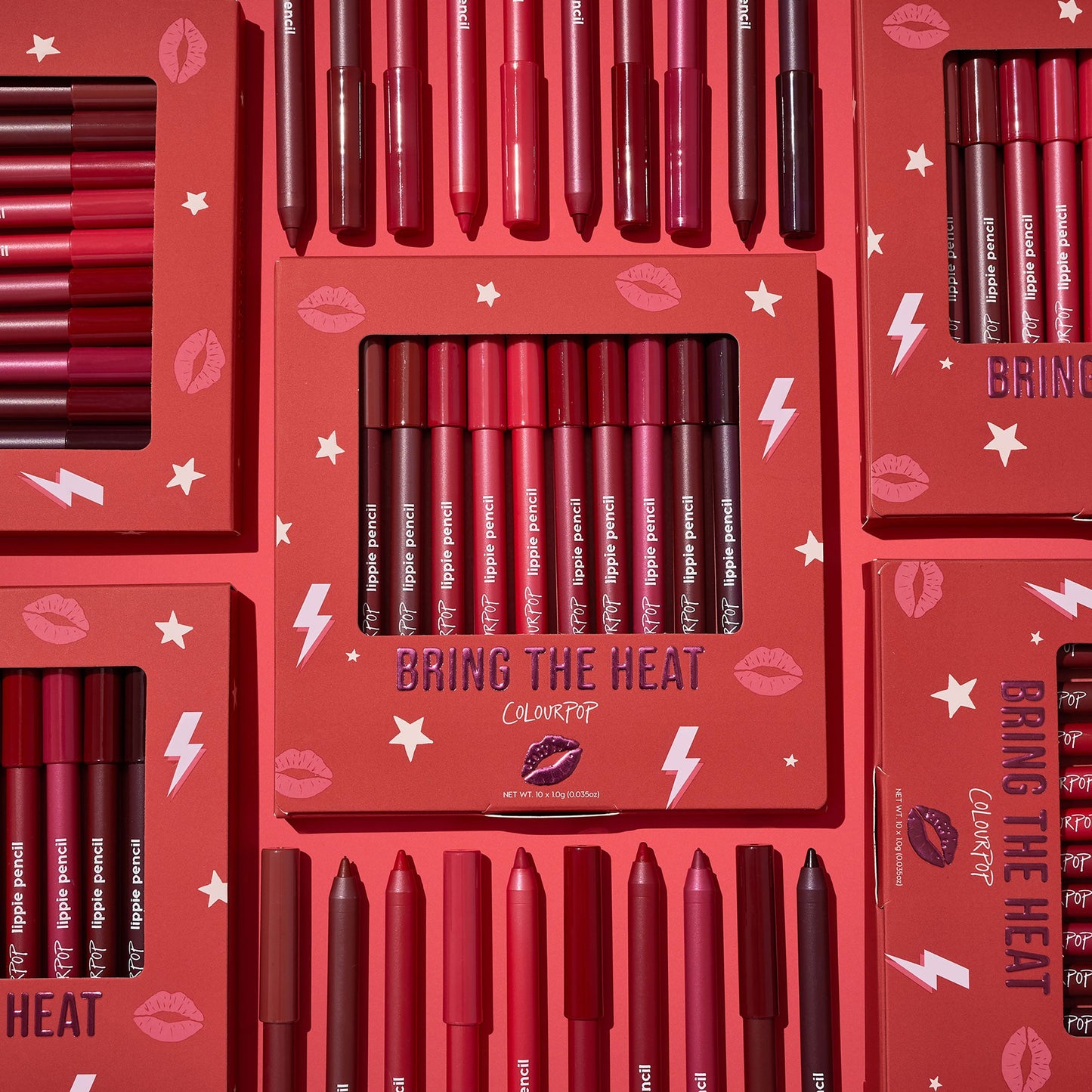 ColourPop Bring The Heat Lippie Pencil set arranged in a flat lay, showcasing creamy lip liners in reds, pinks, and berry tones; boxed and loose pencils surround the main kit on a red background with lips, stars, and lightning graphics.