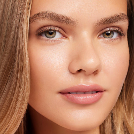 Glossy lips wearing Strawberry Lip Balm by ColourPop Serum Stick, delivering a sheer pink, hydrated finish on a model’s close-up face with natural makeup under soft studio lighting.