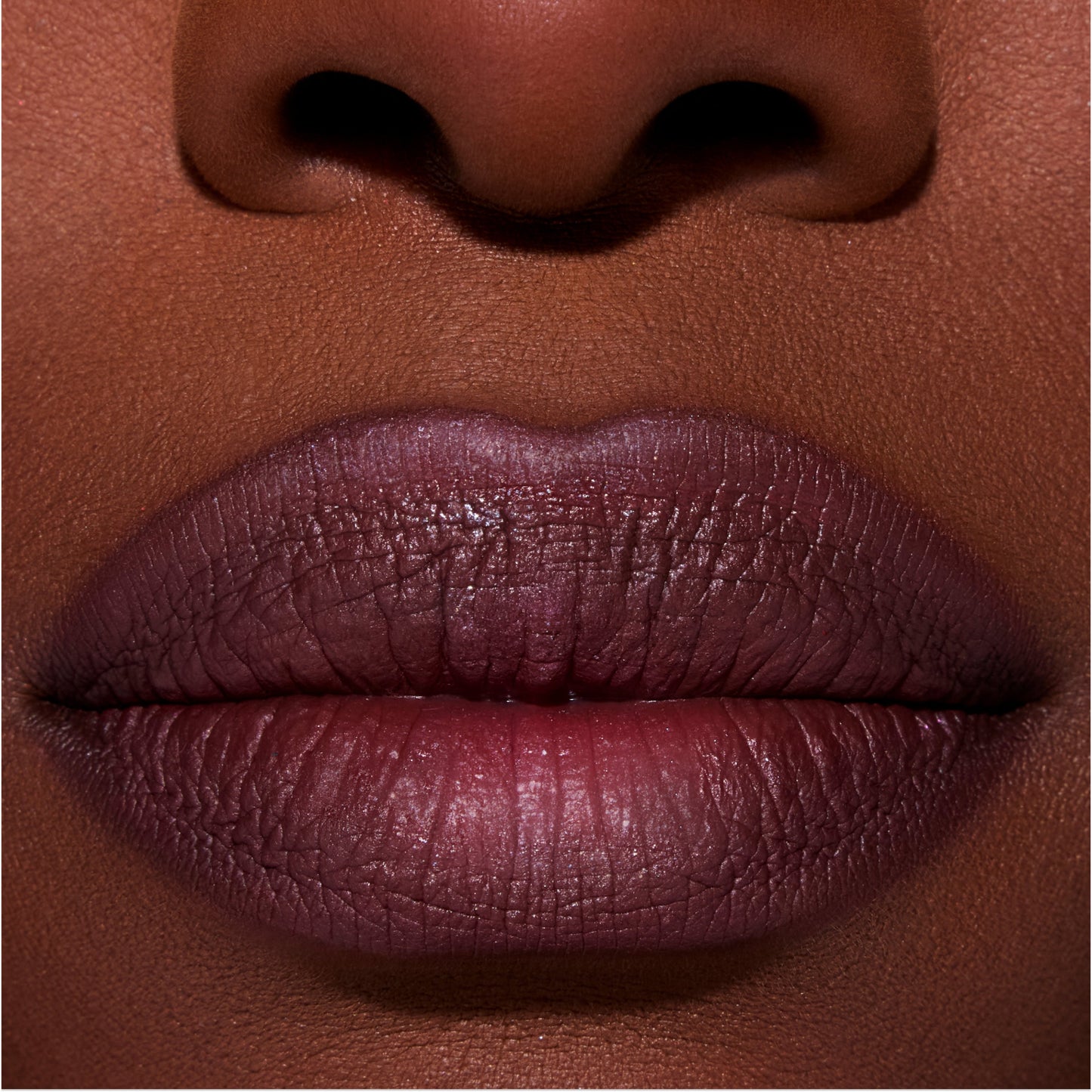 Close-up of full lips wearing ColourPop New Love Lippie Stix in a deep plum Twilight-inspired shade, showing smooth, satin finish color payoff on rich skin tone for a bold, evening makeup look.